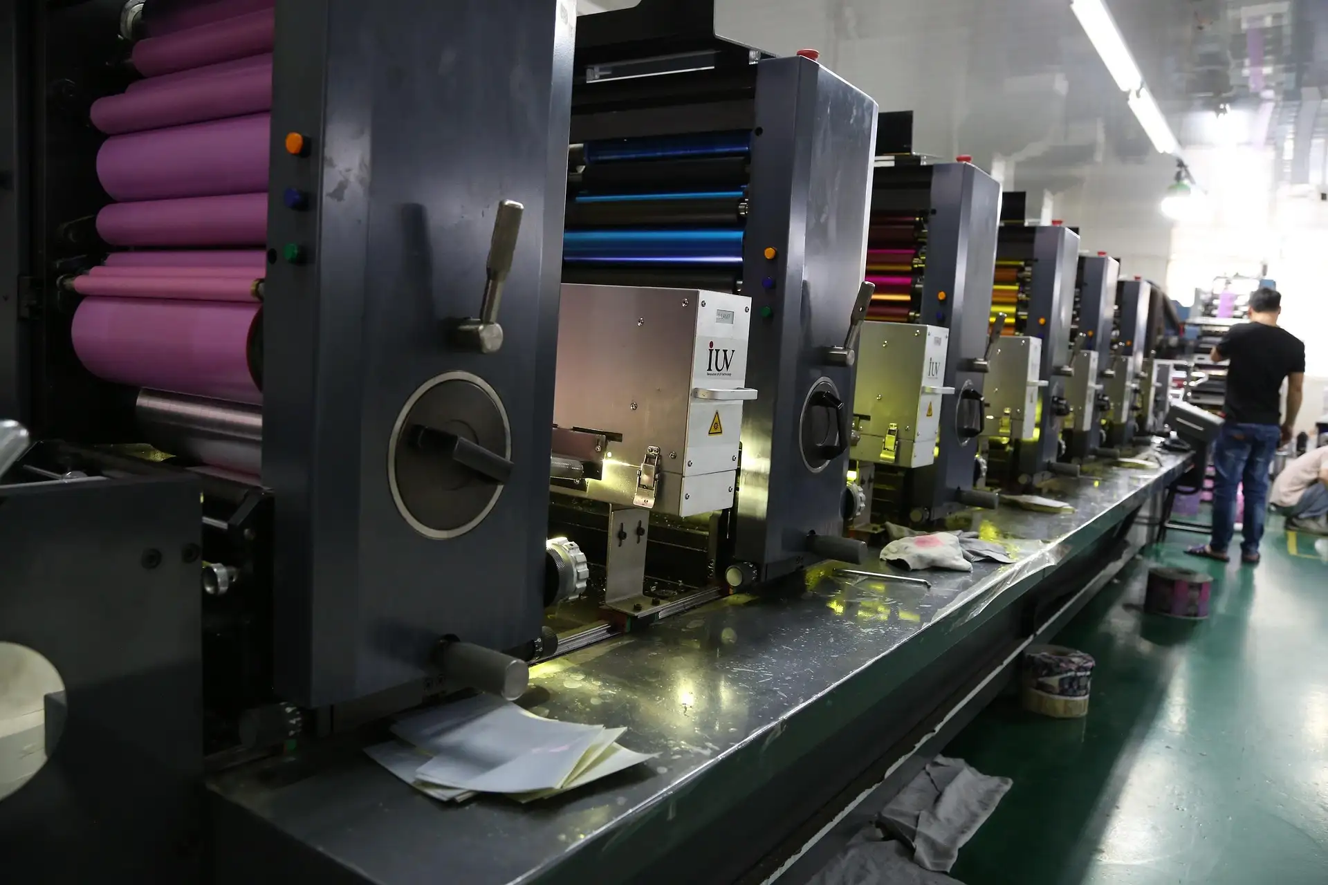 Row of industrial printing machines with colorful rollers in a factory setting.