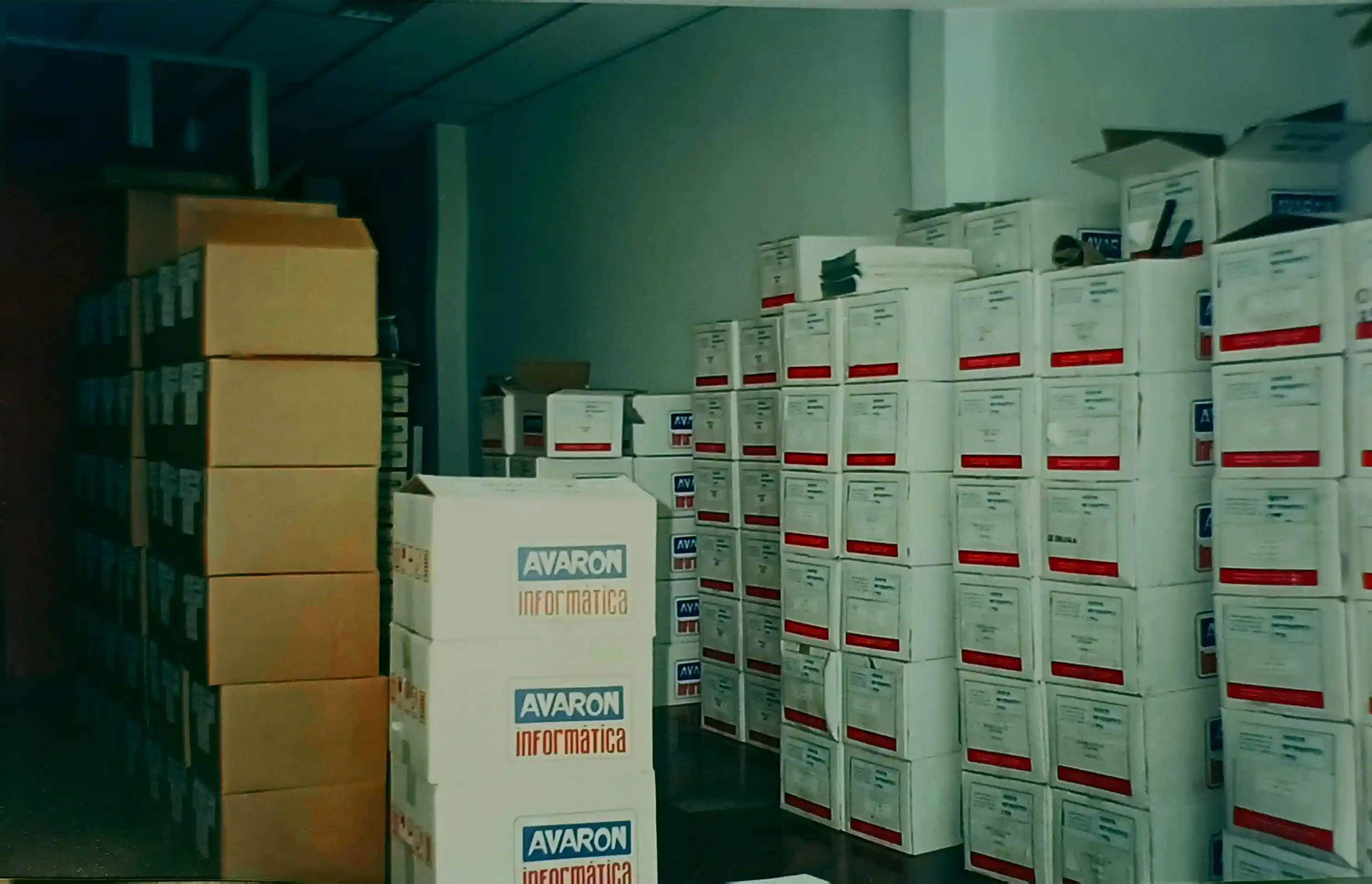 Depósito cheio de pilhas de caixas de papelão, algumas com a identificação Avaron Informática