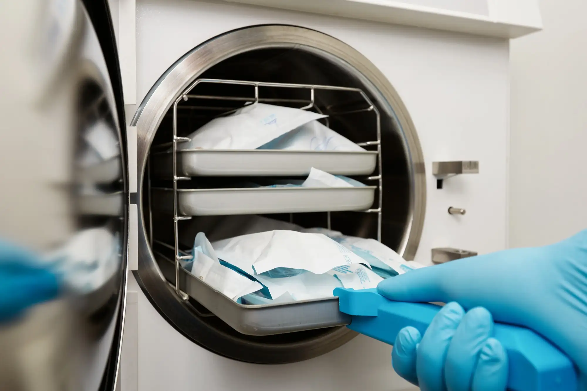 Gloved hand removing sterilized medical instruments from an autoclave machine.