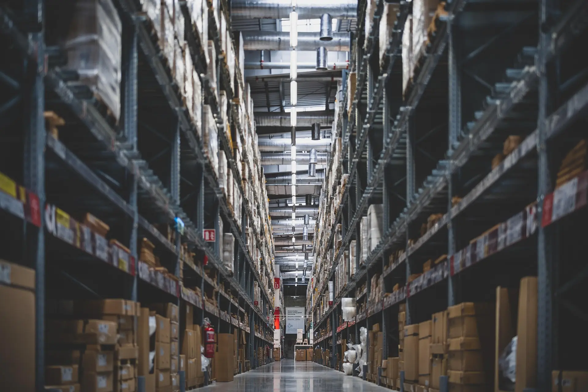 Long aisle in a large warehouse with tall metal shelves stocked with cardboard boxes.